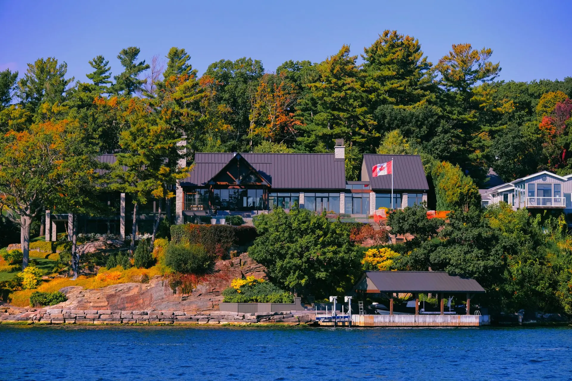 Lakefront home with autumn foliage and Canadian flag in Ontario cottage country